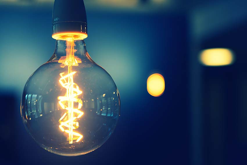 A lit bulb in focus, the filament spiralling inside the glass.