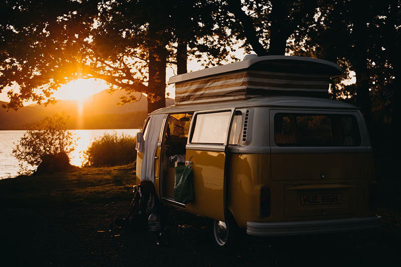 A parked campervan overlooking a lake as the sun sets