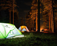 Tents lit up in the forest, with people around a campfire